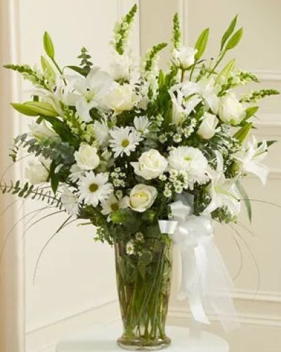<p>Send sympathy, comfort and condolences with this elegant arrangement of fresh white blooms. The hand-designed arrangement of fresh white roses, hybrid lilies and cremones is accented with myrtle, spiral eucalyptus and more and presented in a classic clear glass vase. Have it delivered directly to the funeral home or to the home of the family.</p>