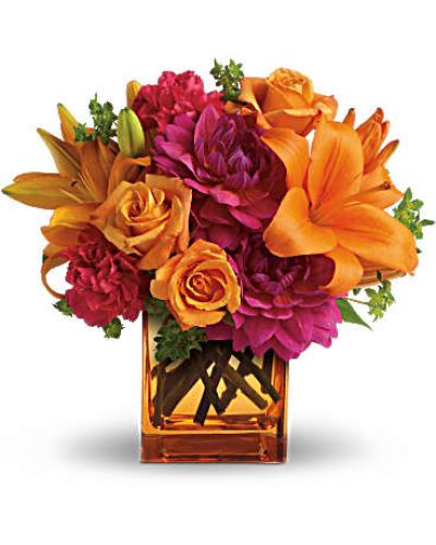 Feeling hot, hot, hot! This sizzling summer floral arrangement mixes hot pink dahlias and carnations with bright orange roses and lilies in an orange cube vase. It&rsquo;s the floral equivalent of a trip to Miami in July!
Light orange roses, orange asiatic lilies, hot pink dahlias and hot pink carnations are presented with fresh green bupleurum in an orange glass cube vase.